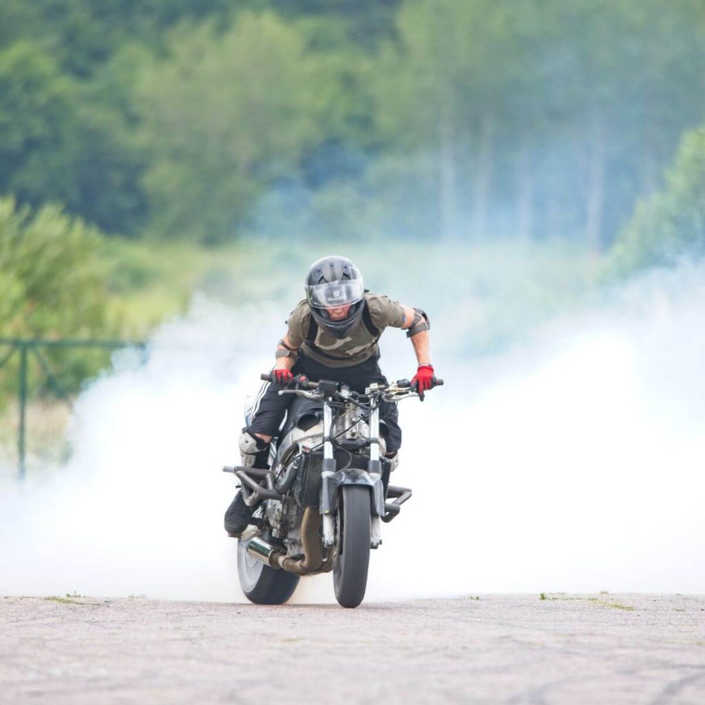 Stunter pali gumę naa swom motocyklu. W tle unosi się chmura dymu.