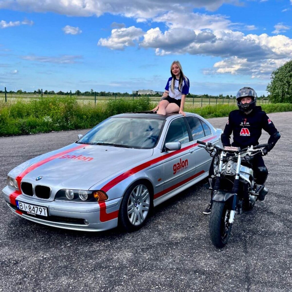stunt. Motocykl do wyczynowej jazdy wraz z kierowcą parkuje obok BMW w barwach Galon Oleje.